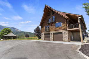 View of side of home with stone siding, log siding, a mountain view, an attached garage, and a balcony