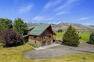 View of property exterior with a lawn, stone siding, a garage, and log exterior