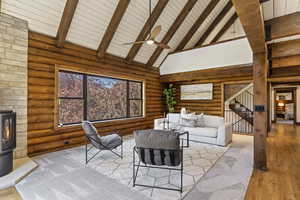Living room featuring a wood stove, light wood-type flooring, a ceiling fan, log walls, and a high wooden beamed ceiling