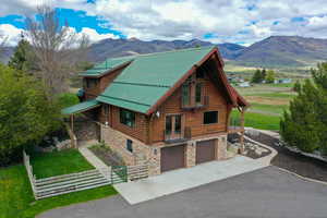 View of side of home featuring log siding, an attached garage, stone siding, a mountain view, and driveway