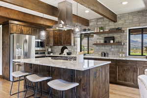 Kitchen with stainless steel appliances, hanging light fixtures, dark wood finish cabinetry, beam ceiling, and a center island