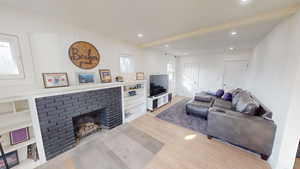 Living area with light wood-style flooring, a fireplace, built in features, recessed lighting, and beam ceiling