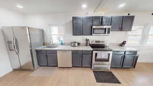 Kitchen with stainless steel appliances, light stone counters, light wood-type flooring, and recessed lighting