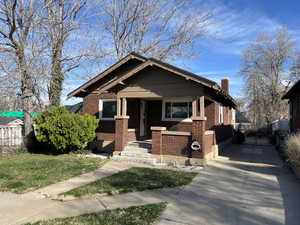 View of front facade with brick siding, a chimney, and covered porch