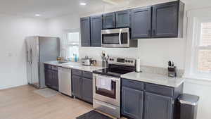 Kitchen with stainless steel appliances, light wood-style floors, light stone countertops, and recessed lighting