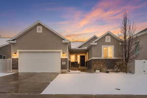 View of front of property with stucco siding, driveway, stone siding, and a garage