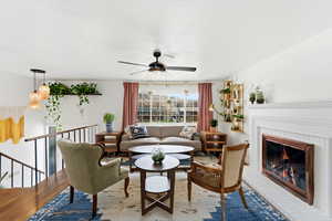 Living area with a brick fireplace, a ceiling fan, and wood finished floors