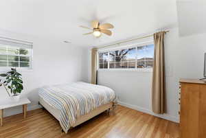 Bedroom with light wood finished floors, multiple windows, and ceiling fan
