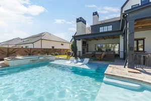 Rear view of house featuring a patio area, a chimney, a fenced backyard, a pool with connected hot tub, and an outdoor bar