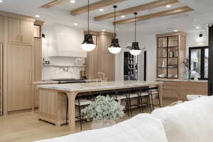 Kitchen with light wood finish cabinetry, decorative backsplash, a breakfast bar, hanging light fixtures, and a raised ceiling