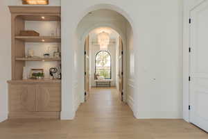 Corridor featuring arched walkways, light wood-style floors, built in features, and suspended lighting