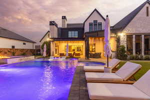 Back of house at dusk featuring a chimney, a patio area, an outdoor lounge area, and a pool with connected hot tub
