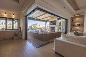 Living room featuring wood-type flooring, a stone fireplace, built in shelves, and ornamental molding