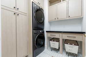 Laundry area with stacked washer and dryer, cabinet space, and light tile patterned flooring