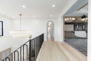 Hall featuring arched walkways, a chandelier, wood finished floors, and an upstairs landing