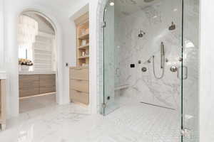 Full bath with a marble finish shower, light marble finish flooring, vanity, and built in shelves