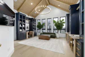 Living area with built in desk, light wood finished floors, a high wood beamed ceiling, and hanging lights