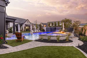 Pool at dusk featuring a patio area, a fenced backyard, and a pool with connected hot tub