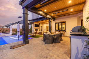 Patio terrace at dusk featuring a large fireplace, area for grilling, a patio area, and an outdoor lounge area with bar