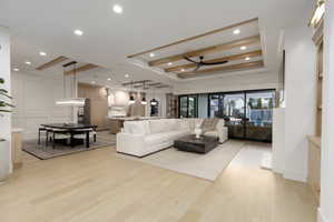 Living area with light wood finished floors, ceiling fan, recessed lighting, and a raised ceiling