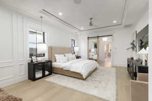 Bedroom with a barn door, light wood finished floors, a raised ceiling, a ceiling fan, and recessed lighting
