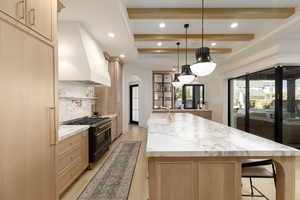 Kitchen with light wood finish cabinetry, light stone counters, double oven range, hanging light fixtures, and beam ceiling