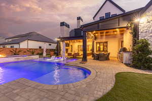 Rear view of house with an outdoor kitchen with living area, a patio, a chimney, a pool with connected hot tub, and a fenced backyard