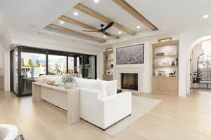 Living area featuring light wood finished floors, crown molding, ceiling fan, arched walkways, and built in features