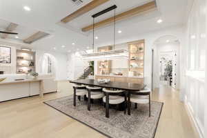 Dining area featuring arched walkways, built in features, light wood-style flooring, a raised ceiling, and recessed lighting