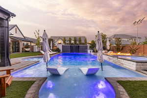 Pool at dusk featuring a patio area, a fenced backyard, and a pool with connected hot tub