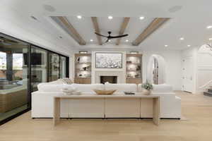 Living area featuring beamed ceiling, a ceiling fan, light wood-style floors, a fireplace, and built in shelves