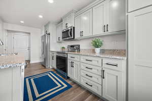 Kitchen featuring stainless steel appliances, light stone countertops, recessed lighting, and dark wood finished floors