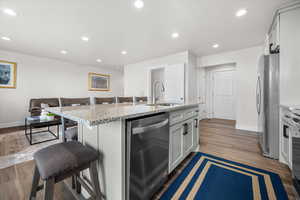 Kitchen with a kitchen breakfast bar, light stone countertops, stainless steel appliances, an island with sink, and recessed lighting