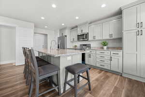 Kitchen with light stone counters, a kitchen bar, a kitchen island with sink, stainless steel appliances, and light wood-style floors