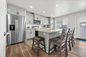 Kitchen with stainless steel appliances, light stone countertops, a breakfast bar area, light wood finished floors, and an island with sink