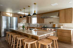 Kitchen with premium appliances, light stone counters, a kitchen breakfast bar, pendant lighting, and dark wood-type flooring