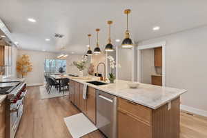 Kitchen with stainless steel appliances, decorative light fixtures, light wood-style flooring, light stone countertops, and wood finish cabinetry