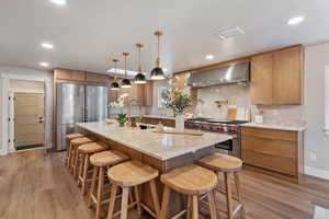 Kitchen featuring light stone countertops, light wood-style floors, decorative light fixtures, premium appliances, and an expansive island