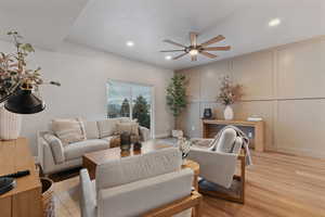 Living room with a decorative wall, light wood-style flooring, a ceiling fan, and recessed lighting
