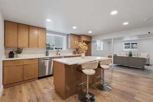 Basement kitchenette with wood finish cabinetry, light wood-style flooring, a kitchen island, stainless steel dishwasher, and recessed lighting