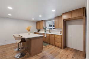Basement kitchenette featuring wood finish cabinets, light wood finished floors, a breakfast bar area, a center island, and recessed lighting