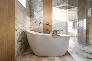 Full bathroom featuring healthy amount of natural light, a freestanding bath, and stone wall