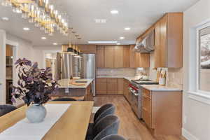 Kitchen with light stone countertops, light wood-style floors, stainless steel appliances, oversized fridge, decorative light fixtures, and extractor fan