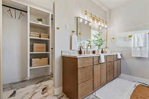 Bathroom with double vanity, light marble finish floors, and a closet