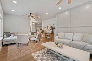Living area with a ceiling fan, light wood-style floors, a decorative wall, and suspended lighting