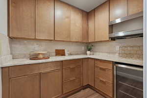 Pantry with wine cooler, light stone countertops, tasteful backsplash, wood finish cabinetry, and light wood finished floors