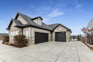 View of front of home with stone siding, board and batten siding, a shingled roof, concrete driveway, and a garage