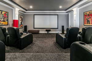 Home theater room with a tray ceiling, ornamental molding, dark carpet, recessed lighting, and ornate columns