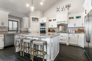 Kitchen with lofted ceiling, white cabinets, stainless steel appliances, a kitchen breakfast bar, and a kitchen island