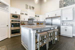 Kitchen with white cabinetry, stainless steel appliances, a breakfast bar area, dark wood-style floors, and a high ceiling